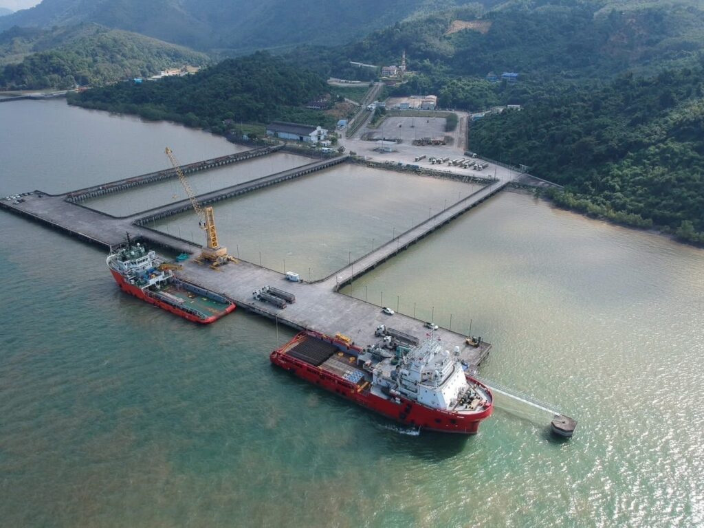 Two red support vessels moored beside a long pier in a bay